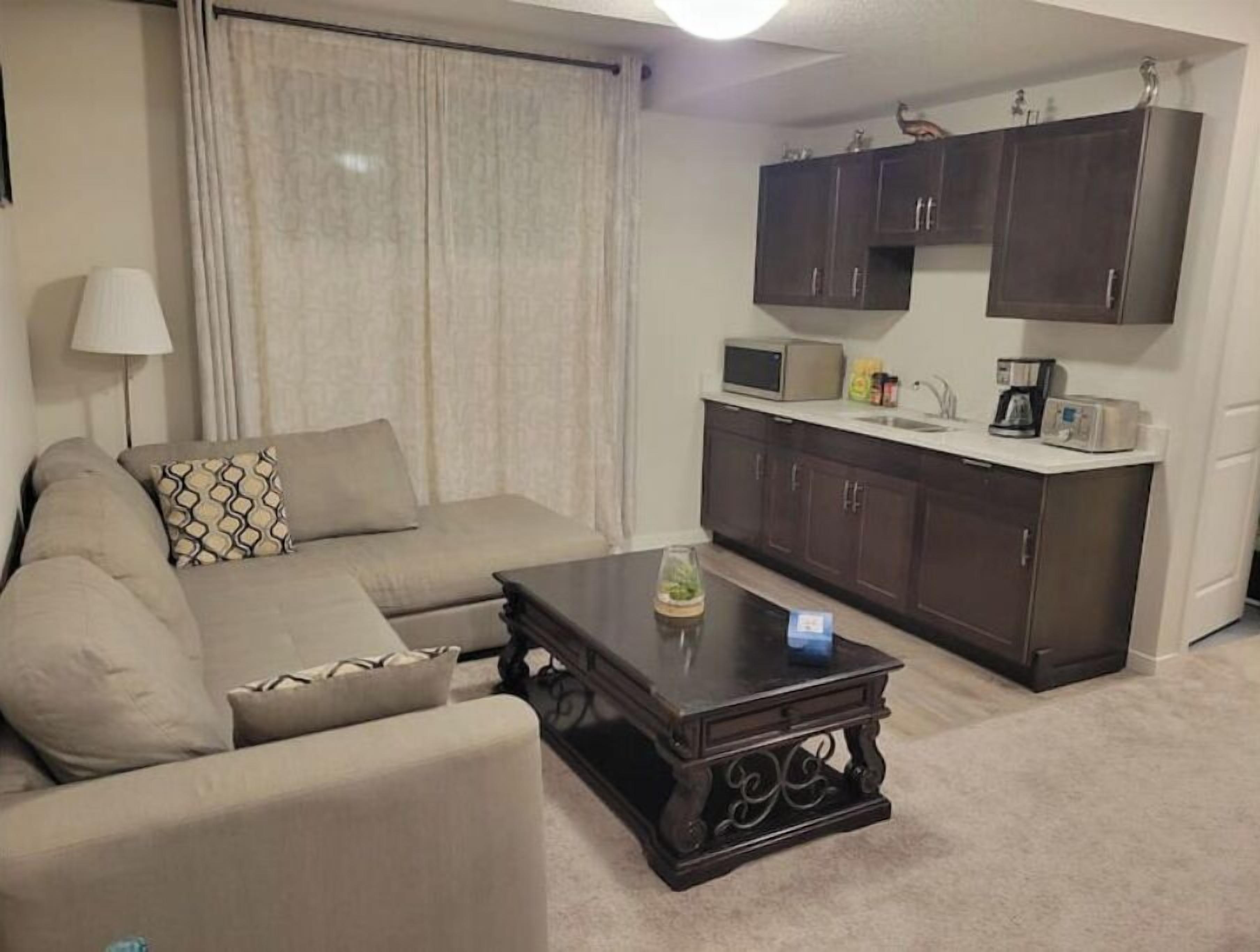 A living room with a sofa, a coffee table, and a kitchen area with cabinets and appliances.