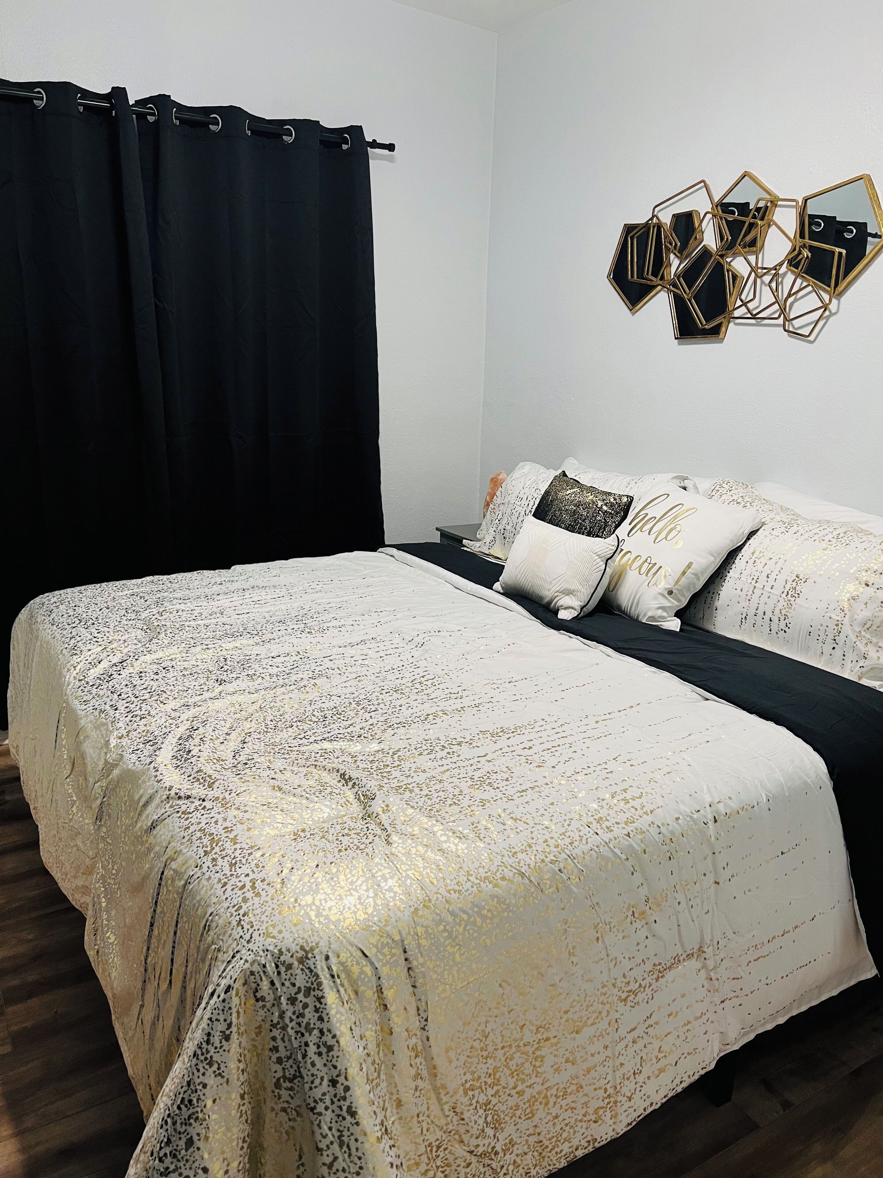 Un dormitorio con cama, cortinas negras, un espejo en la pared y almohadones decorativos.