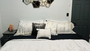A bedroom with a bed, a nightstand, a decorative wall piece, and a door.