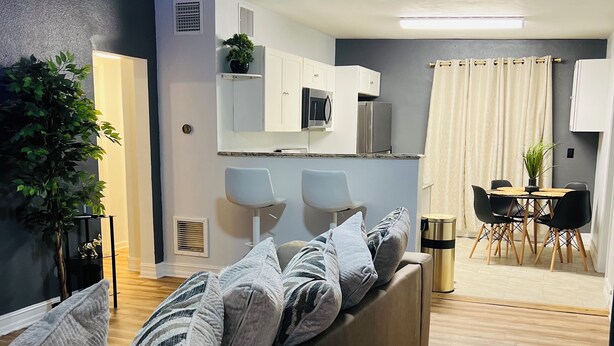A modern living room with a sofa, a ceiling fan, and a dining area with a table and chairs.
