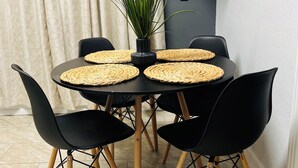 A round dining table with four black chairs, a potted plant, and woven placemats.