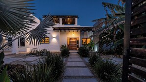 A modern house with a stone pathway leading to the entrance, surrounded by tropical plants. - Casa Alas. Newly built, private pool, and a short walk to the beach! (Todos Santos)