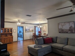 Ein geräumiges Wohnzimmer mit einem grauen Ecksofa, Holzschränken und einem Essbereich mit Stühlen und einem Tisch.