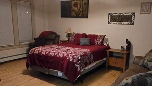 A bedroom with a bed, a nightstand, a dresser, a sofa, and a ceiling light. - Cozy, yet spacious studio apt. (Hibbing)