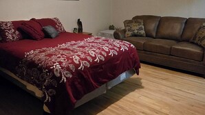 A bedroom with a bed, a wooden floor, a ceiling fan, and a brown leather sofa. - Cozy, yet spacious studio apt. (Hibbing)