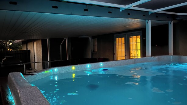 An indoor swimming pool with a tiled edge, a ceiling with recessed lighting, and a door with illuminated glass panels.