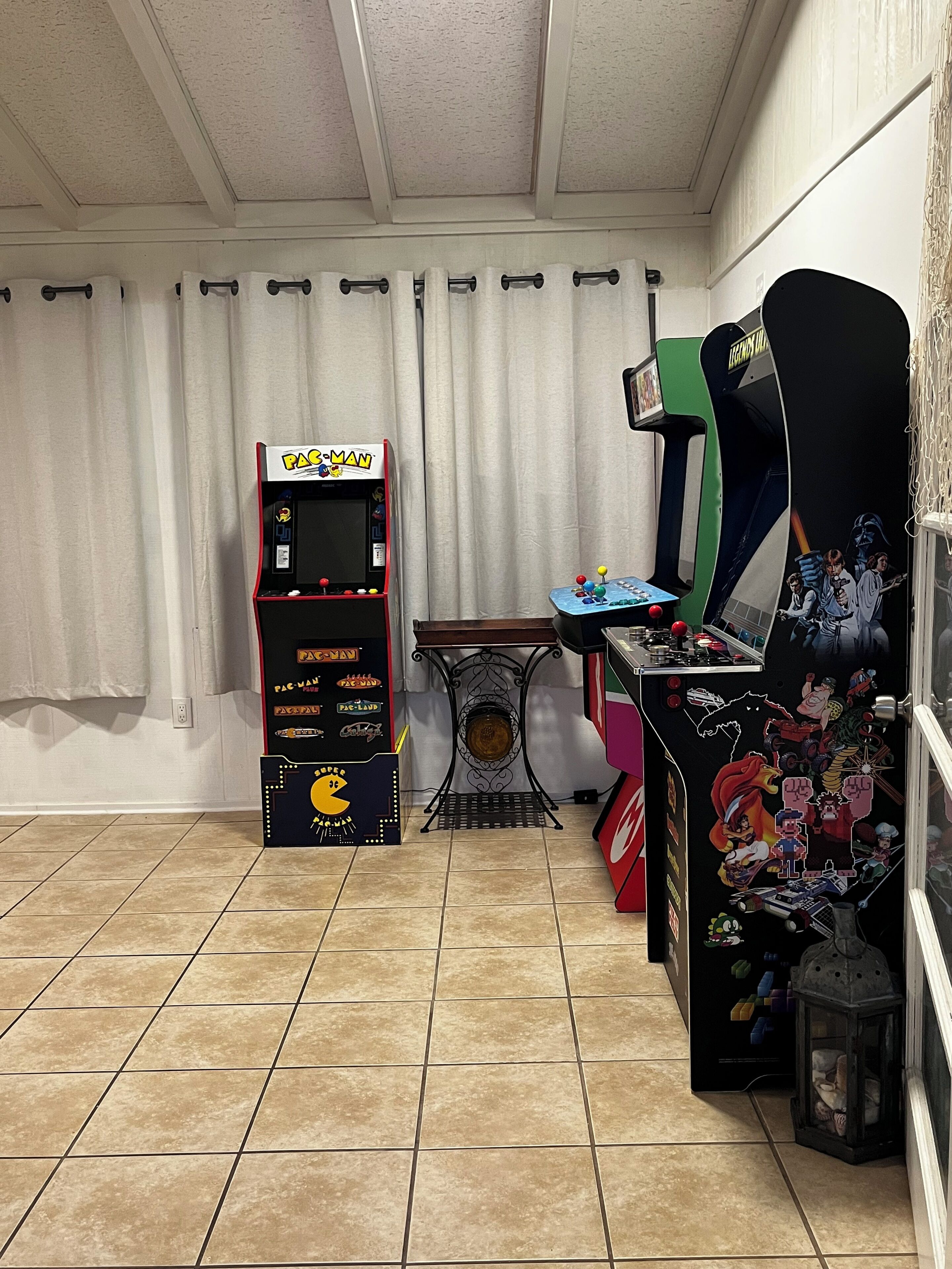 Una habitación con una máquina arcade de Pac-Man, una mesa de pinball y una pared decorada con diversos adhesivos.