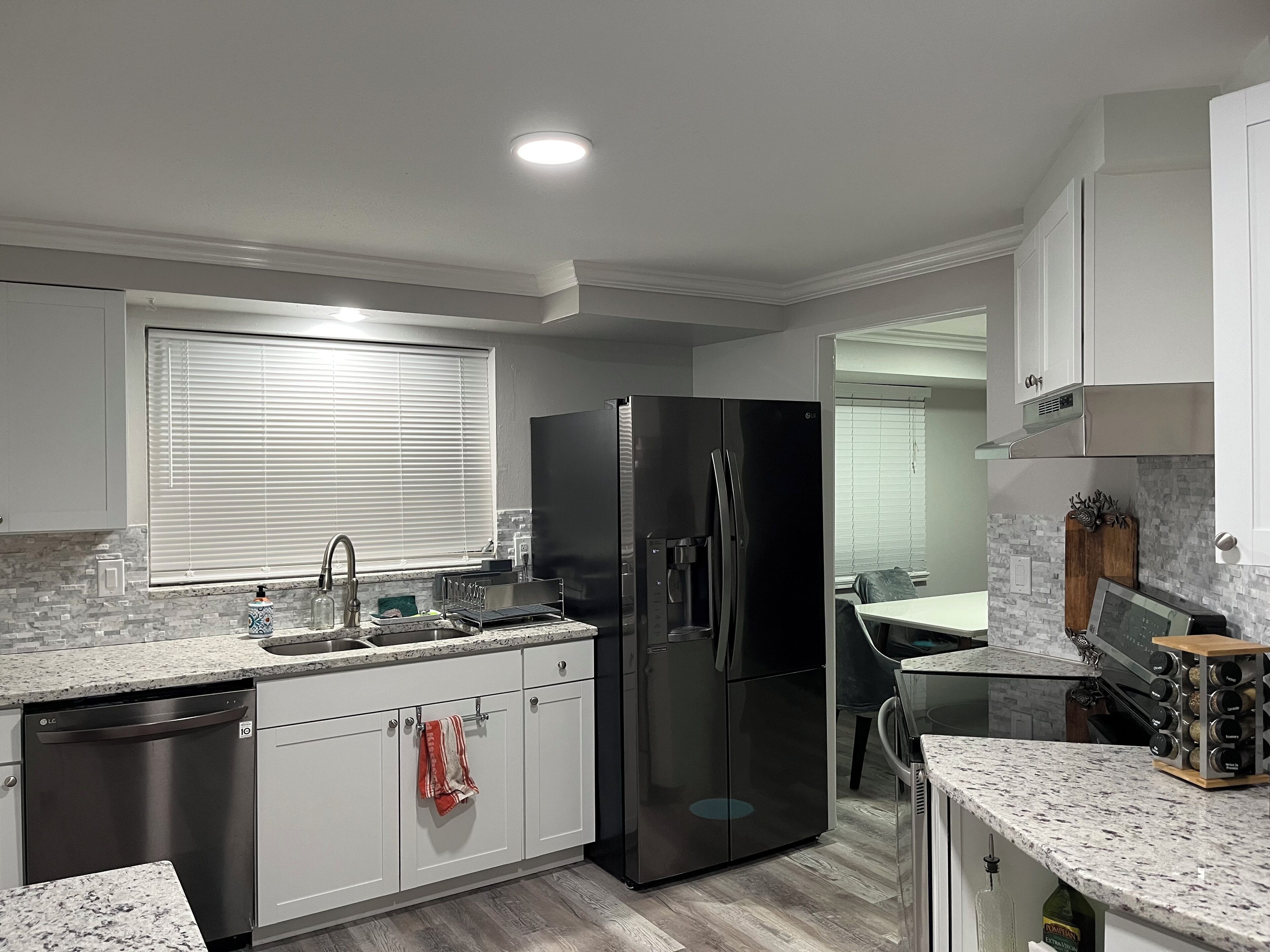 A modern kitchen with a black refrigerator, white cabinets, and a granite countertop.