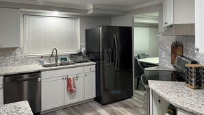 A modern kitchen with a black refrigerator, white cabinets, and a granite countertop.
