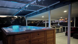 A hot tub with LED lights, wooden benches, and a barbecue grill under a covered patio.
