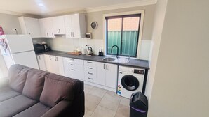 A compact kitchen with white cabinets, a built-in washing machine, and a window with a view of a brick wall. - A Little Southern Comfort - granny flat in Sanctuary Point  (Sanctuary Point)