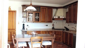 A kitchen with wooden cabinets, a dining table with chairs, a hanging light fixture, and a tiled backsplash. - La Culla Tra I Vigneti - Stanza (Grazzano Badoglio)