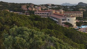 Uma vila costeira com edifícios rodeados de vegetação e uma grande formação rochosa ao fundo.