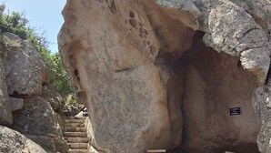 Formação rochosa com uma mesa, cadeiras, uma placa e uma escadaria.