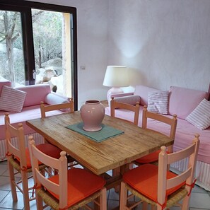 A cozy room with a wooden dining table, pink upholstered chairs, and a sofa with striped cushions.