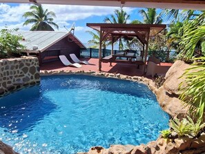 A clear blue pool with lounge chairs, a wooden deck, and a gazebo. - Bungalow Cosy, Calme et Reposant (Tahaa)