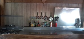 Una cocina con estufa a gas, un lavamanos de acero inoxidable y diferentes utensilios y botellas.