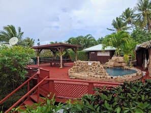 A pool area with a stone wall, a wooden deck, and a gazebo. - Bungalow Cosy, Calme et Reposant (Tahaa)