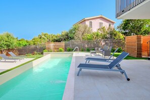 Una piscina con sillas de descanso, una valla de madera y un edificio al fondo.