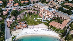 Vista aérea de un complejo turístico costero con un edificio grande, una playa y un área de piscina.