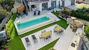 Una casa moderna de dos plantas con piscina, mobiliario exterior y una escalera que conduce al nivel superior.