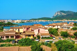 Un pueblo costero con edificios de tejas color terracota, un puerto deportivo y una montaña al fondo.