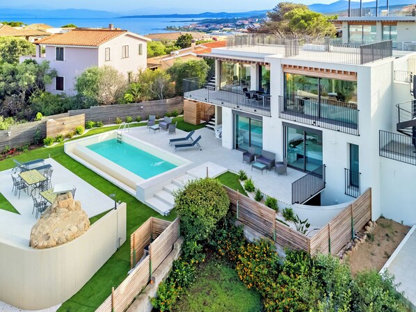 Una propiedad residencial moderna con piscina, mobiliario exterior y vista al mar.