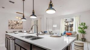 A modern kitchen with a large island, pendant lighting, and a view to the living area. - Stunning Themed Home, Private Pool, Ideal Location (Kissimmee)