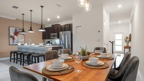 A modern kitchen with dark cabinets, a stainless steel refrigerator, and pendant lighting. - Stunning Themed Home, Private Pool, Ideal Location (Kissimmee)