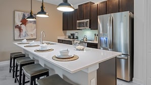 A modern kitchen with a central island, stainless steel appliances, and dark wooden cabinets. - Stunning Themed Home, Private Pool, Ideal Location (Kissimmee)