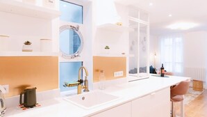 Eine moderne Küche mit weißer Arbeitsplatte, einer Spüle und einem runden Spiegel. Auf der Arbeitsplatte steht eine kleine Pflanze und eine Wasserflasche.
