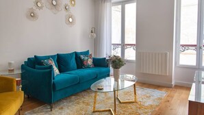 Ein Wohnzimmer mit einem blaugrünen Sofa, einem Glastisch und einem gelb gemusterten Teppich.