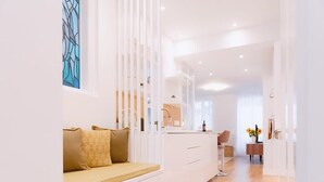 Ein modernes, helles Zimmer mit einem weißen Sofa, einem Essbereich und einer Küche im Hintergrund.