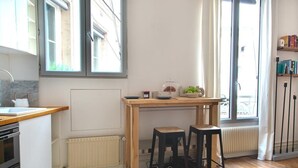 A modern kitchen with a wooden table, two stools, a radiator, and a window with curtains. - Le Plaisir du Pantheon + Seine Cruise (Aug only!) (Paris)
