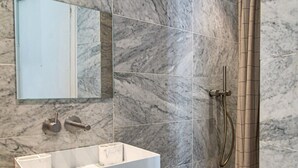 A bathroom with a marble-tiled wall, a white sink with two soap dispensers, a mirror, and a shower with a handheld showerhead. - Le Plaisir du Pantheon + Seine Cruise (Aug only!) (Paris)