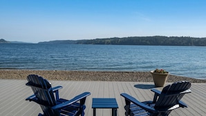 Een terras met Adirondack-stoelen en een tafel, met uitzicht op een kalm meer, en een bebost eiland in de verte.