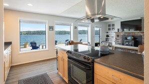 Een moderne keuken met een groot eiland, een inbouwoven en uitzicht op het water.