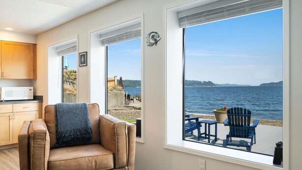 Een kamer met een groot raam met uitzicht op een strand, een bruine leren fauteuil en een klein tafeltje met een potplant.