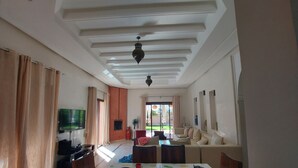 A spacious living room with a dining area, a TV, and a ceiling fan. - Villa de Charme , Piscine Privée, Calme (Oulad hassoune - Marrakech)