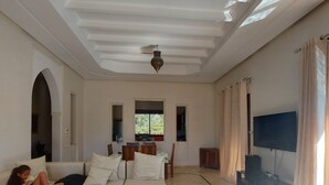 A spacious living room with a high ceiling, a large TV, and a comfortable seating area including a sofa and a red armchair. - Villa de Charme , Piscine Privée, Calme (Oulad hassoune - Marrakech)