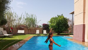 A swimming pool with a tiled deck, surrounded by a grassy area and a few lounge chairs. - Villa de Charme , Piscine Privée, Calme (Oulad hassoune - Marrakech)