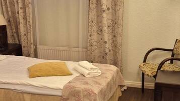 A room with two beds, a chair, and a window with curtains.