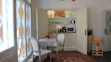 Una cocina compacta con armarios blancos, un microondas y una cafetera. Hay una mesa de comedor con dos sillas y un florero con flores.