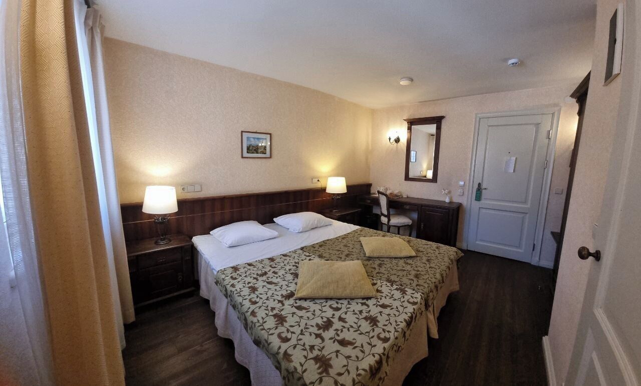 A hotel room with a bed, two bedside tables, a desk, a chair, a mirror, and a door.
