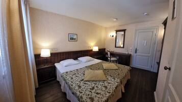A hotel room with a bed, two bedside tables, a desk, a chair, a mirror, and a door.