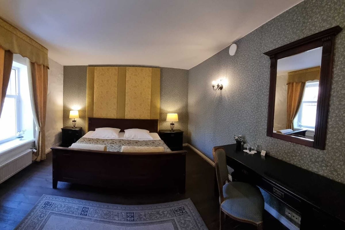 Une chambre d’hôtel avec un grand lit, deux lampes de chevet, une commode, une chaise et un miroir.