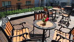 Eine Holzterrasse mit Gartenmöbeln, darunter Bänke und Tische, umgeben von einem Metallgeländer.