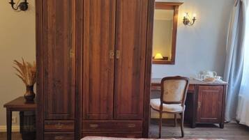 A bedroom with a large wooden wardrobe, a chair, a desk with a lamp, and a bed with a floral bedspread.