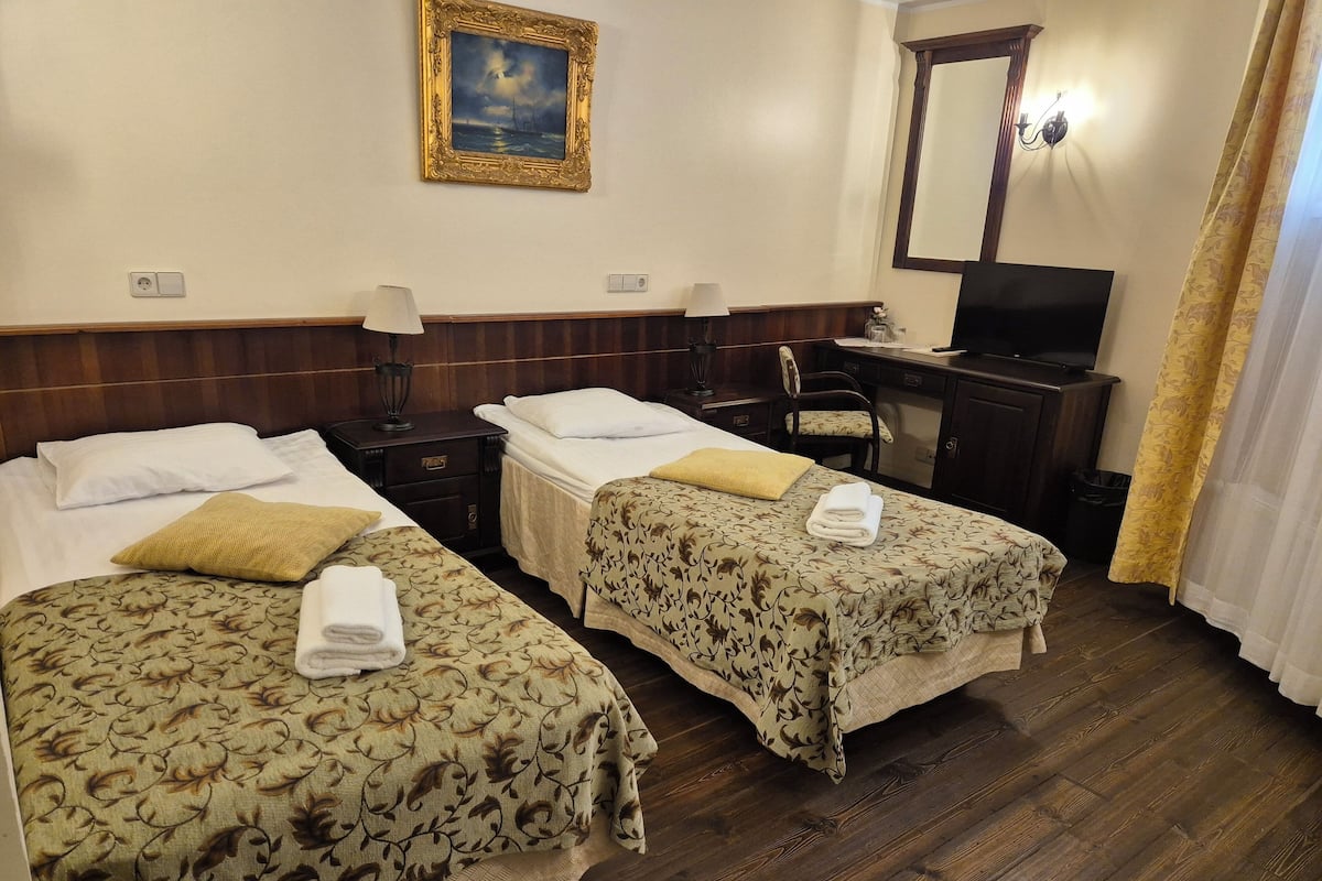 Une chambre d’hôtel avec deux lits simples, un bureau avec une chaise, une télévision et un tableau au mur.