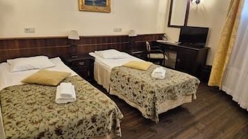 A hotel room with two single beds, a desk with a chair, a television, and a painting on the wall.